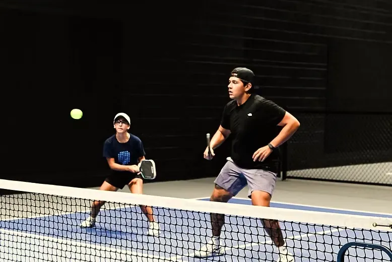 Two players at the net mid-rally on an indoor court at The Grove